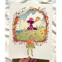 Risograph print of a small witch girl sitting on a green hilltop with a cloudy blue sky behind. She holds a broom and has a hand radio, with a black cat laying beside her. Scene is framed by a wreath made of bread, flowers and birds.