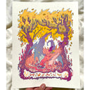 A hand holds a white art print featuring a whimsical illustration of a forest with a large pink dragon creature, yellow-orange trees, and purple accents.