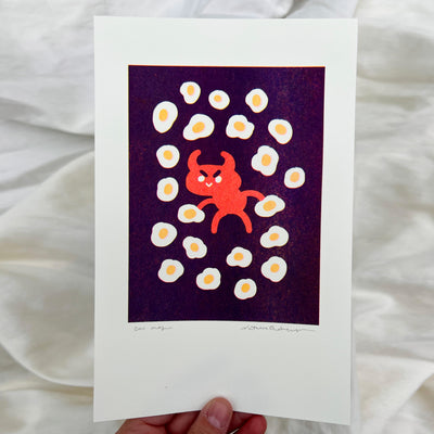Risograph print of a cartoon devil with a simple evil smiling face, standing and holding a sunny side up egg in each hand. All around are sunny side eggs, on a dark purple background.