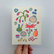 Cream colored greeting card with colorful doodles on the front. Drawings include fruit, a sea shell, glasses, a pencil, vase and flowers.  