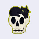 Die cut sticker of a cream colored stylized skull, with a smiling black cat with green eyes resting atop of it. A thin bright green outline is around the skull and cat.