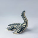 Black matte ceramic sculpture of a Loch Ness Monster with a sea turtle body and a long neck, with cream colored line carvings on its body and neck and a poppy flower design on its back.