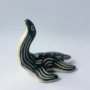 Black matte ceramic sculpture of a Loch Ness Monster with a sea turtle body and a long neck, with cream colored line carvings on its body and neck and a poppy flower design on its back.