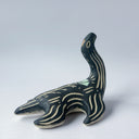 Black matte ceramic sculpture of a Loch Ness Monster with a sea turtle body and a long neck, with cream colored line carvings on its body and neck and a poppy flower design on its back.