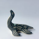 Black matte ceramic sculpture of a Loch Ness Monster with a sea turtle body and a long neck, with cream colored line carvings on its body and neck and a poppy flower design on its back.