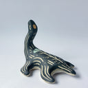 Black matte ceramic sculpture of a Loch Ness Monster with a sea turtle body and a long neck, with cream colored line carvings on its body and neck and a poppy flower design on its back.