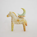 Horse figurine, painted cream with yellow color accents and sparkle shapes on it. Atop its back is a crescent moon resting on a flower.