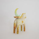 Horse figurine, painted cream with yellow color accents and sparkle shapes on it. Atop its back is a crescent moon resting on a flower.