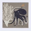 Gray square handkerchief with an illustration of a navy blue octopus, holding a small piece of orange coral. It has one of its tentacles loosely wrapped around a large white coral plant.