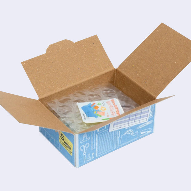 Open box of miniature stickers, made to resemble a shipping box with bubble wrap around the product and a small invoice. Exterior of box looks like realistic office supply box.