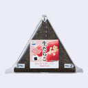 A packaged triangular onigiri eraser snack with a pink and white label in Japanese, showing dark seaweed rice inside, photographed on a light gray background.