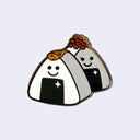Enamel pin of 2 onigiri rice balls, one has a tiny fish atop it and the other has roe. They both have cute, cartoon smiles and a sparkle on their seaweed wrapping.