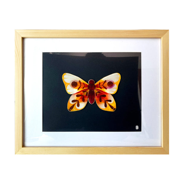 Painting on cut out paper of a butterfly with burgundy, yellow and deep orange coloring. Its wings have abstract leaf shape patterns with a circle in the center of each top wing. Butterfly is mounted on black paper in a light grain wood frame with a white mat.