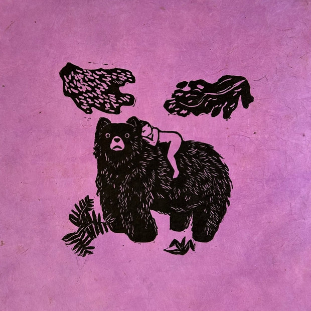 Black ink linocut print on pinkish purple fibrous paper of a small nude woman laying atop of a black bear. Bits of greenery are around the pair.