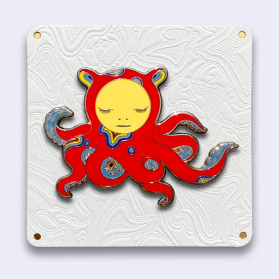 Die cut enamel pin designed by James Jean, of a red octopus with sparse blue and yellow swirl patterning, and a circular human like face, looking down. Its many arms are curled into itself and have blue tentacles.