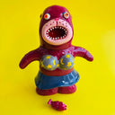 Burgundy painted seal-like soft vinyl figure, standing with colorful eyes, an open mouth and wearing a star pattered gray bikini and blue skirt.