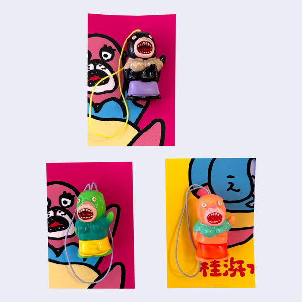 3 small vinyl figurines of sea lion creatures, with their mouths open showing many small teeth. They are dressed in crop tops and skirts and each have one hand up.