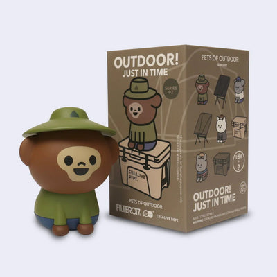 Toy figure of a bear in outdoor gear next to its packaging on a light gray background