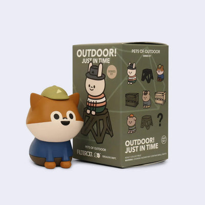 Toy figure of a cartoon dog or fox with a hat next to its packaging.