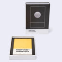 PANTONE Yellow 012 card holder shown with its black-and-white branded box standing behind it and an open tray in front displaying the yellow card inside.