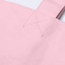 Close-up of a light pink canvas tote bag showing the fabric texture, stitching, and part of the strap against a white background.