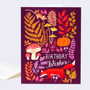 Greeting card with autumn-themed illustrations and 'Birthday Wishes' text on a purple background.