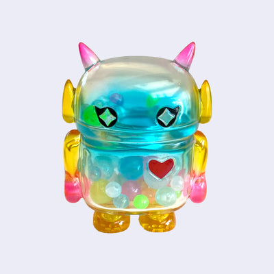 Pastel rainbow colored soft vinyl figure with colorful round beads inside. Figure is shaped like a smaller Big Boss Robot, with a bigger head than normal and two black eyes with sparkles as pupils. A red heart is on its upper right chest.