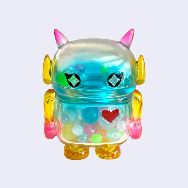 Pastel rainbow colored soft vinyl figure with colorful round beads inside. Figure is shaped like a smaller Big Boss Robot, with a bigger head than normal and two black eyes with sparkles as pupils. A red heart is on its upper right chest.