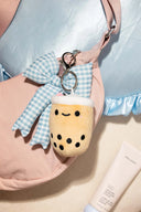 Plush keychain of a boba drink with a cute cartoon face, attached to a pink bag with a blue and white gingham bow.