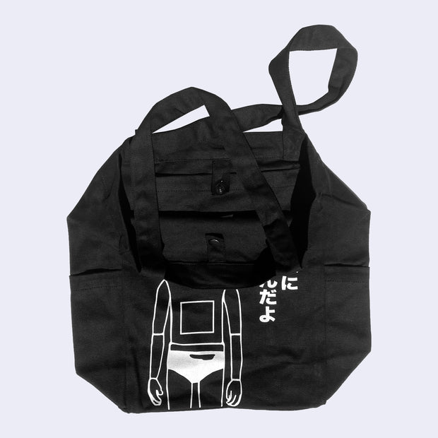 Black tote bag with interior slightly shown, displaying a snap button to close the top of the tote bag.