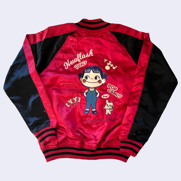 Back view of the red bomber jacket with a large embroidery of Peko Chan, a smiling girl with pigtails and overalls. Words read "Newflash Peko" and "Pop Candy" and "How much do you like this milk candy?"