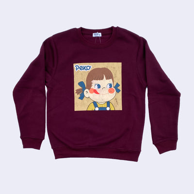 Deep burgundy colored sweatshirt with a square graphic of Peko Chan, a small smiling cartoon girl with rosy cheeks and a tongue out. She has blue bows in her hair and wears a yellow shirt and jean overalls. The graphic is weathered purposefully.