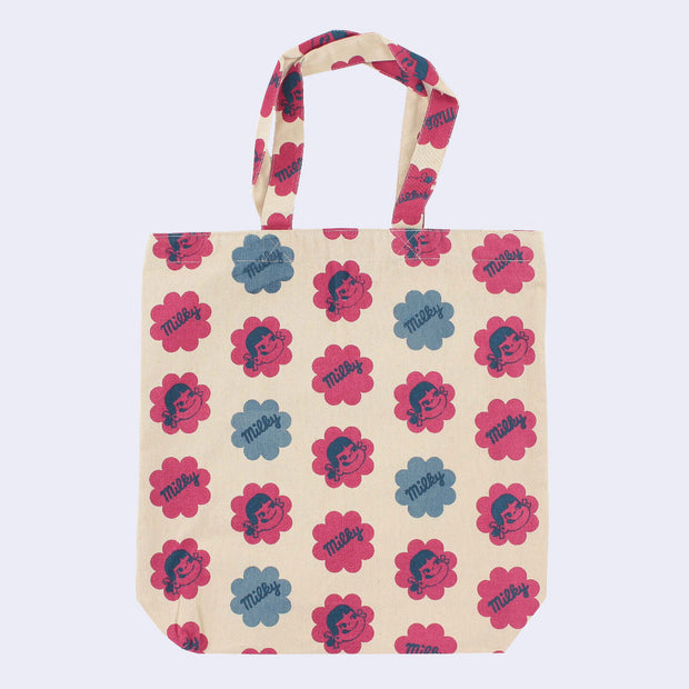 Cream colored tote bag featuring a pattern of large flower shaped blocks of red and blue, faded stylistically. One diagonal row features illustrations of Peko Chan's smiling face, and the next row features text that reads "Milky" within the flowers. Row pattern alternates between designs.