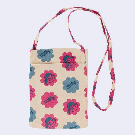 Small pouch like bag with a long, thin should strap. Bag is cream colored with a pattern of large flower shaped blocks of red and blue, faded stylistically. One diagonal row features illustrations of Peko Chan's smiling face, and the next row features text that reads "Milky" within the flowers. Row pattern alternates between designs.
