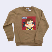 Warm tan colored sweatshirt with a square graphic of Peko Chan, a small smiling cartoon girl with rosy cheeks and a tongue out. She has blue bows in her hair and wears a yellow shirt and jean overalls. The graphic is weathered purposefully.