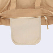Close up of a tan tote bag with a zip closure top, showing a cream colored inner pocket in addition to the main storage area within the tote.