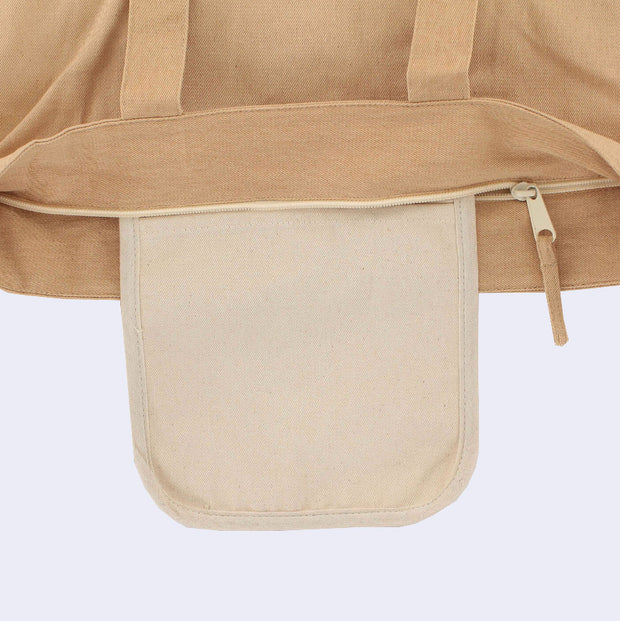 Close up of a tan tote bag with a zip closure top, showing a cream colored inner pocket in addition to the main storage area within the tote.