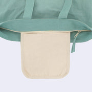 Close up of a teal tote bag with a zip closure top, showing a cream colored inner pocket in addition to the main storage area within the tote.