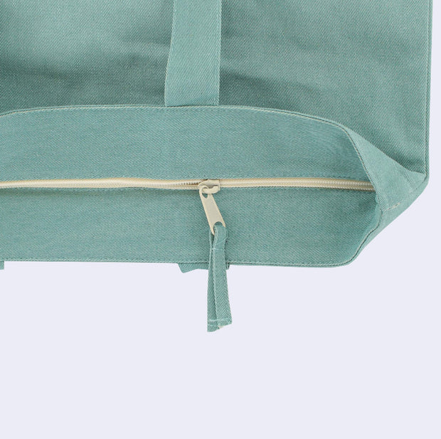 Close up of a zip top teal tote bag, featuring the cream colored lined zipper.