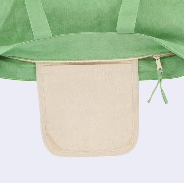 Close up of a green tote bag with a zip closure top, showing a cream colored inner pocket in addition to the main storage area within the tote.