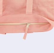 Close up of the top of a pink tote bag, displaying a cream colored zip closure.