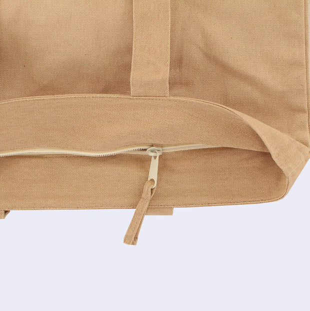 Close up, showing a tan tote bag with a zipper closure at the top.