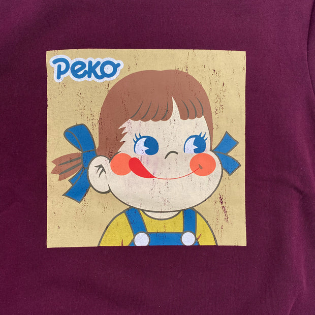 Deep burgundy colored sweatshirt with a square graphic of Peko Chan, a small smiling cartoon girl with rosy cheeks and a tongue out. She has blue bows in her hair and wears a yellow shirt and jean overalls. The graphic is weathered purposefully.