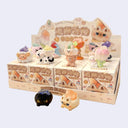 Several figurines made to look like they are carved out of wood and then painted, each holding a crystal on its back and standing in front of its product packaging.