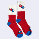 A pair of socks, mostly red, with cream coloring at the top and blue toe and heel color accents. A small graphic of a pill capsule is on the side of the socks.