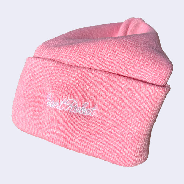 Side view of a pink beanie with white embroidered cursive that reads "giant robot"