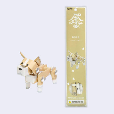 Paper sculpture of a corgi, made out of folded paper pipes. It stands next to its tan product packaging.