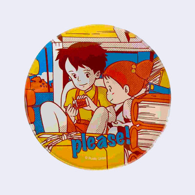 Circular small glass plate with bright colors: Yellow, orange and blue. Featuring a vintage style illustration from My Neighbor Totoro of 2 young girls behind packages and books and sharing candy. Text on the plate reads "Please!"