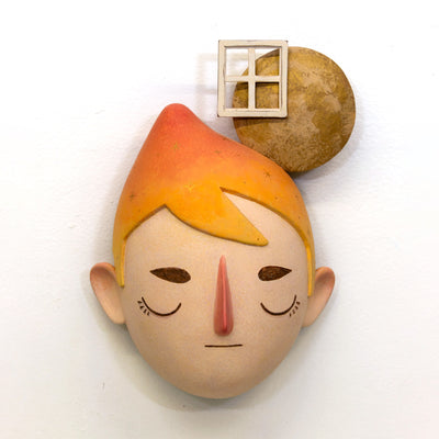 Sculpture of a person's head with a solemn yet sweet expression. They have orange hair and atop their head is a moon with a window.