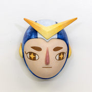 Sculpture of a person's head with a solemn yet sweet expression. They wear a helmet like a superhero with blue stripes and a large yellow arrow.